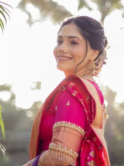 A beautiful profile shot capturing the bride's serene expression against a soft, sunlit background. Her elegant hair bun and the details of her blouse sleeve are beautifully featured here.