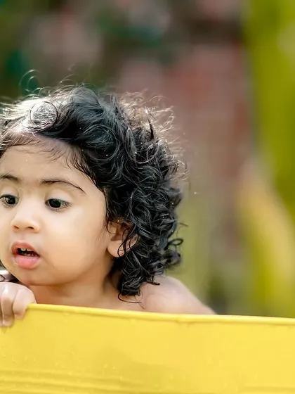 A close-up of a little girl with gorgeous curls, peeking over the edge of the tub.