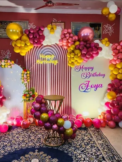 An elaborate home birthday decoration with multiple arched backdrops. The rich color palette of magenta, yellow, and white balloons creates a festive and full look.