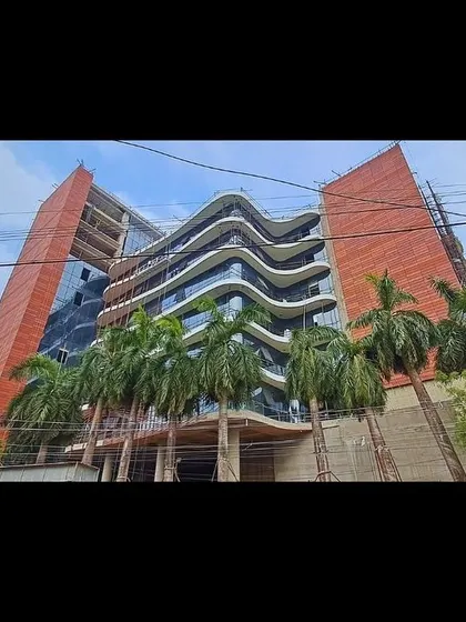 A low-angle view of Peerless Hospital during construction, highlighting the expressive, wave-like form of the balconies against the solid brick-clad towers.