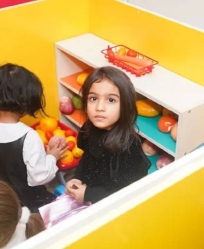 A girl plays in a yellow cubby, part of our imaginative play structures.