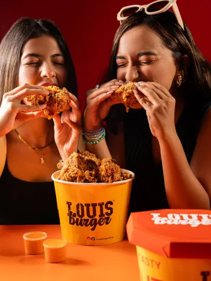 A follow-up shot of the models enjoying the Louis Burger fried chicken, focusing on the satisfying moment of the first bite.