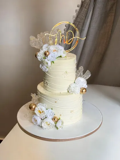 A bride envisioned a minimalist design with a touch of elegance, and this two-tier beauty was the result. Crafted in classic white with delicate gold accents and a custom initial topper, it’s simply timeless.