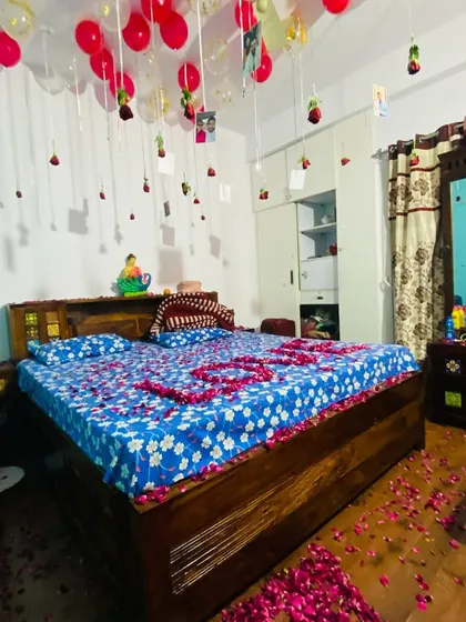 A romantic room setup with photos and roses hanging from the ceiling balloons, and the word "LOVE" spelled out with petals on the bed.