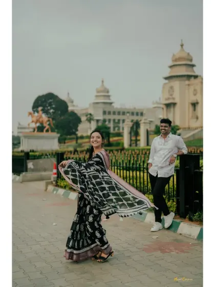 A playful and candid shot of a bride twirling her saree on a city sidewalk, with her partner looking on with a smile.