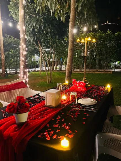 I arrange intimate, romantic dinners for two in any outdoor setting. This garden setup includes a fully set table with a red runner, rose petals, a classic candelabra, and ambient lighting from surrounding LED candles and overhead string lights.