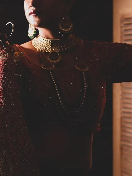 A close-up shot focusing on the bride's outfit and jewelry, captured with dramatic lighting. This image highlights the texture and details of her bridal attire.