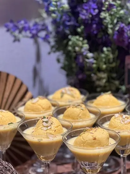 A modern presentation of Rasmalai, served in elegant martini glasses. The creamy, saffron-infused milk and soft cheese dumplings are garnished with nuts.