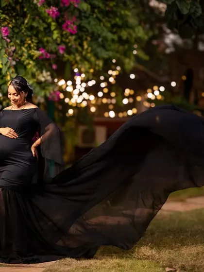 The flowing black fabric creates a sense of motion and drama against the garden backdrop and bokeh lights.