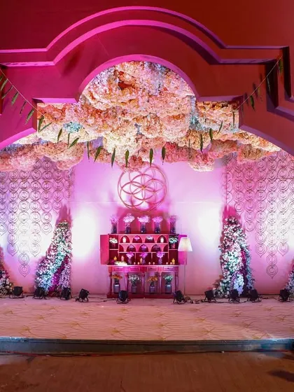 A grand archway frames the view into the 'Anant' themed event space, with a stunning floral cloud overhead and intricate decor drawing guests into the celebration.