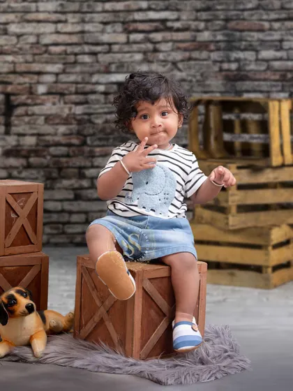 A curious toddler takes a seat on a wooden crate against a rustic brick wall. This simple, textured setup is perfect for capturing natural and candid baby portraits.
