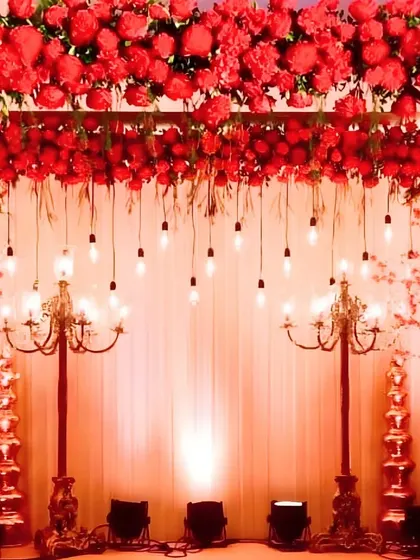 A dramatic and romantic stage bathed in red light, featuring a canopy of red flowers, hanging Edison bulbs, and ornate candelabras for a vintage glam look.