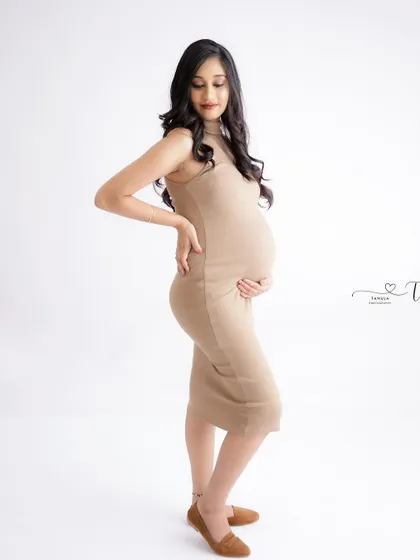 A chic and minimalist side-profile portrait. The mom-to-be's simple beige dress beautifully highlights her baby bump.
