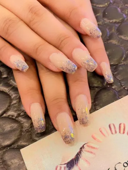 Long, square-shaped nails with a sheer nude base and a dusting of iridescent blue and purple glitter at the tips. A simple yet enchanting design.