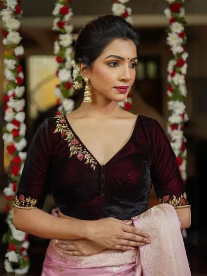 A model wears a deep red velvet blouse with delicate floral embroidery, paired with matching traditional earrings.