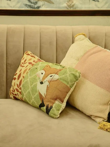 A close-up shot of the upholstery detail on a custom curved sofa. The image highlights the soft, channel-tufted fabric and the playful, decorative cushions that add a touch of whimsy.