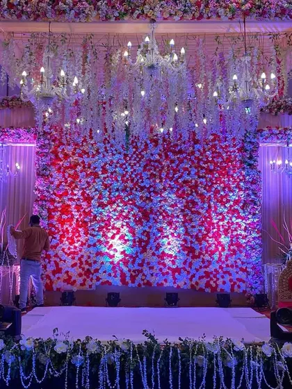 An indoor mandap or small stage with a stunning backdrop of red and white flowers and hanging crystal chandeliers.