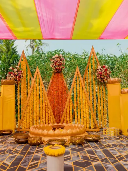 The geometric marigold stage stands ready for the Haldi ceremony, with colorful pink and yellow drapes overhead.