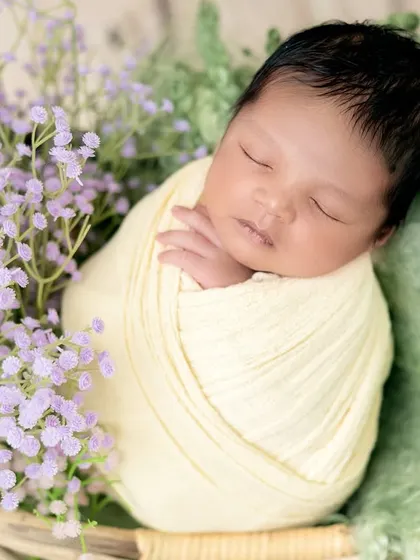 A newborn swaddled in soft yellow, nestled in a basket with fresh lavender flowers. The combination of yellow and purple creates a beautiful, gentle color palette.