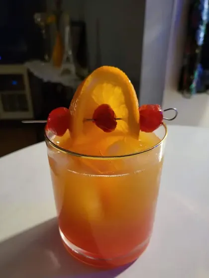 A classic Tequila Sunrise mocktail. The beautiful gradient of orange and red makes it a visually stunning drink, garnished simply with an orange slice and cherries.