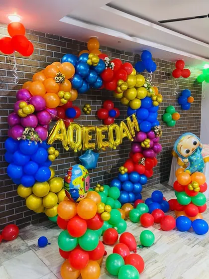 A vibrant Cocomelon themed birthday decoration with a circular balloon frame. The setup uses primary colors and includes Cocomelon character foil balloons.