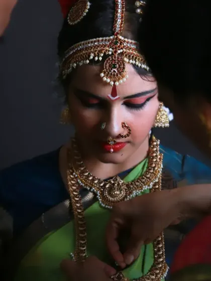 A behind-the-scenes candid from the Arangetram shoot, showing the dancer getting help with her intricate jewelry. These "getting ready" moments are filled with quiet emotion and anticipation.