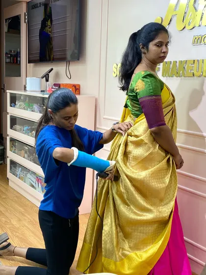 A trainer showing a student how to drape a saree in the traditional Madisar style.