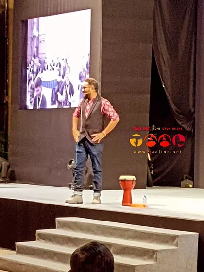 A facilitator on stage at a business conference, with a single djembe. It's a testament to how little you need to create a powerful, unifying experience for a large audience.