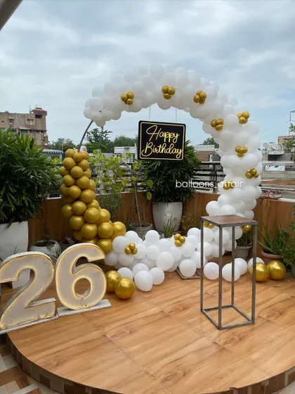 An elegant and modern 26th birthday setup on a rooftop terrace. This decoration features a stylish white and gold balloon semi-arch, large marquee light-up numbers, and a custom 'Happy Birthday' sign, perfect for a chic outdoor celebration.