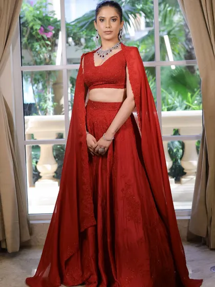 A full-length view of the red cocktail outfit with a dramatic cape. The makeup is kept sleek and monotone to balance the boldness of the attire.