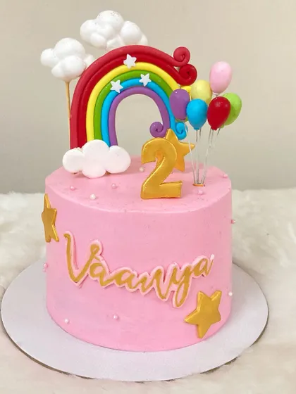 A sweet pink cake for a 2nd birthday, decorated with a vibrant rainbow, fluffy clouds, and colorful balloons.