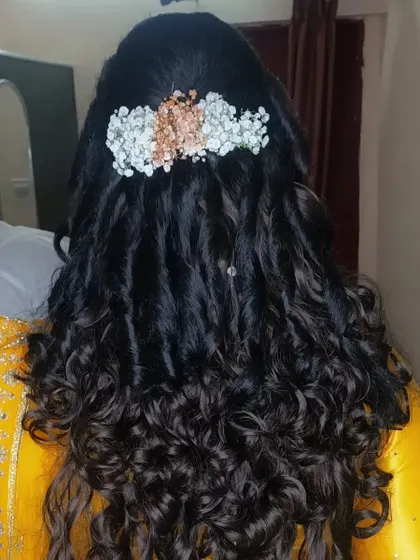 A beautiful curly hairstyle perfect for a reception or sangeet. The curls are soft and bouncy, and the look is finished with a delicate arrangement of fresh flowers.