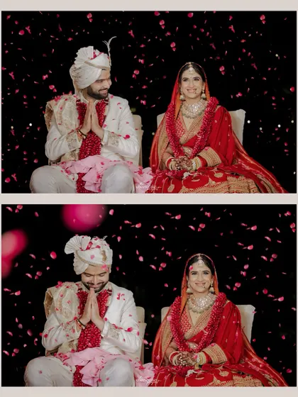 A formal portrait of the couple seated after their Pheras, with a shower of petals against a dramatic black background.