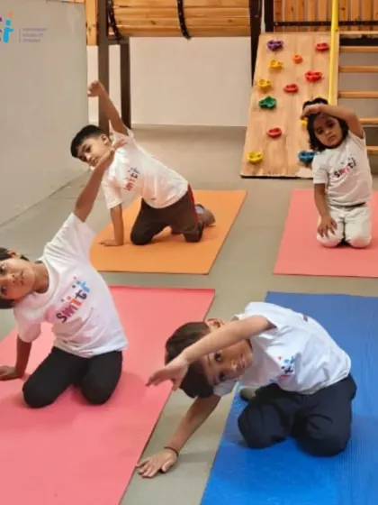 Children practice a seated side-stretch, improving their flexibility and coordination. Our indoor play area is also used for physical activities.