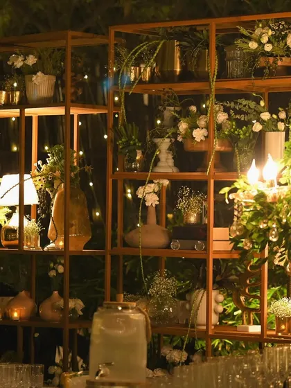 A beautifully styled shelving unit used as a backdrop for the bar. It's filled with a curated collection of vases, floral arrangements, and candles, adding depth and interest to the space.