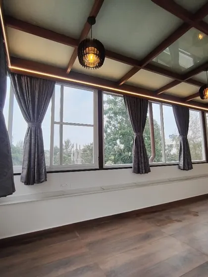 An elegant and functional indoor space created with a glass pergola roof. The combination of large windows, a transparent roof, and rich wood flooring makes the room feel bright, airy, and connected to the outdoors.