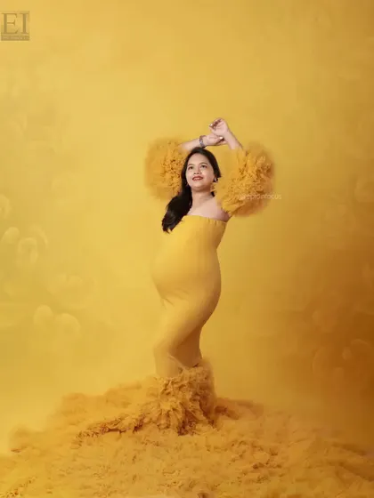 A vibrant studio portrait with the mom-to-be in a sunshine-yellow gown, her arms raised in a joyful pose.