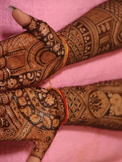 A close-up of the hands, showing the fine details of the bridal mehandi, including peacocks and floral patterns.
