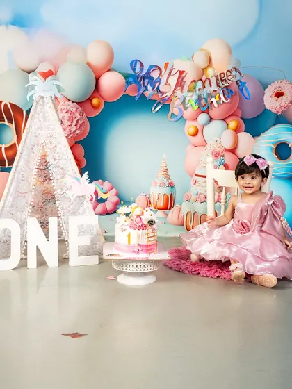 This little princess is ready for her first birthday party! The pink dress and festive donut-themed backdrop create a perfectly sweet and celebratory atmosphere.