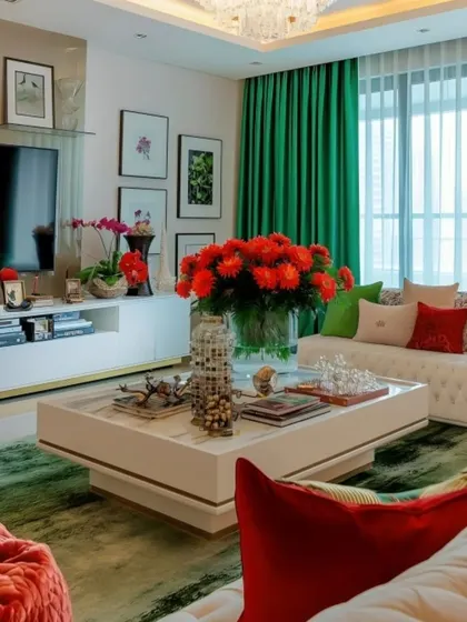 This living room is a vibrant mix of colors and textures, featuring a comfortable white sofa accented with green curtains and bold red floral arrangements. The gallery wall above the TV adds a personal and artistic touch to the space.
