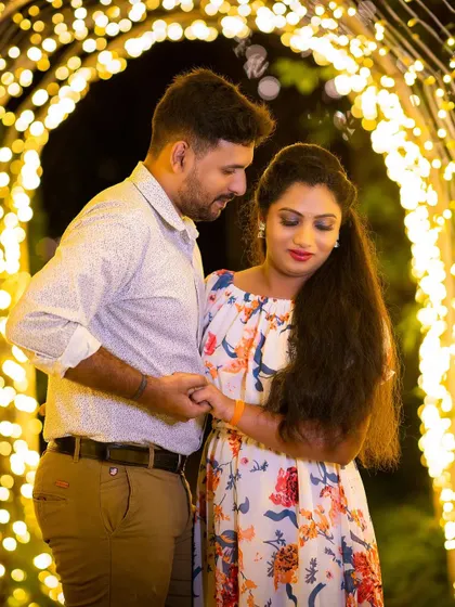 An intimate pre-wedding portrait of a couple under an arch of glowing lights.