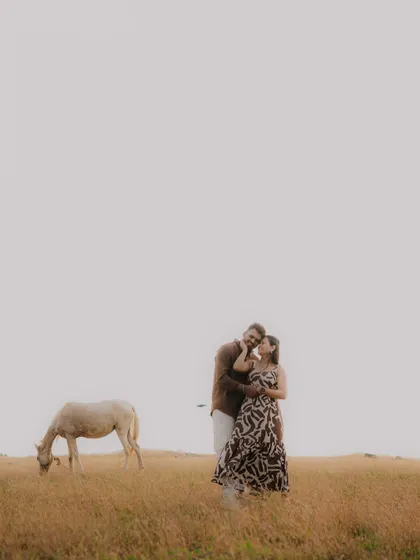 A wide, minimalist shot of a couple in a vast, golden field, with a horse grazing nearby. This image has a peaceful, storybook quality, emphasizing the couple's connection within a beautiful, expansive landscape.