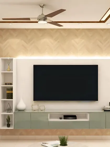 A floating TV console in a soft green finish is the highlight here, set against a herringbone-patterned wood wall. The design includes a slim open shelf on one side for a balanced, asymmetrical look.
