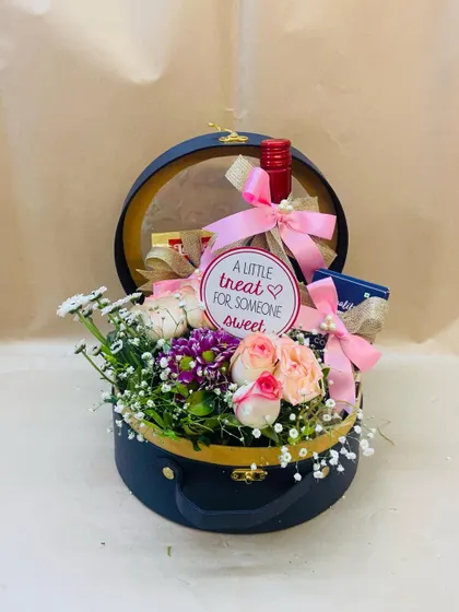 A little treat for someone sweet. This charming round gift box includes a small bottle of wine and chocolates, nestled among a bed of fresh flowers.