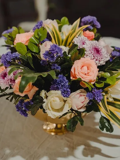 A close-up of a vibrant floral centerpiece, featuring a mix of roses, chrysanthemums, and other colorful blooms in a golden vase.