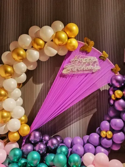A closer view of the purple and white circular balloon arch. The "Happy Birthday" neon sign is placed creatively on the purple fabric drape.