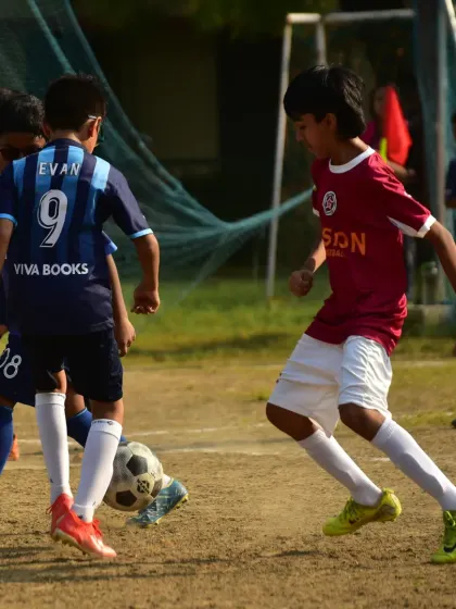 A player skillfully maneuvers the ball between two opponents, demonstrating the close control and composure we develop.