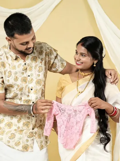 A happy couple reveals they are expecting a girl with a tiny pink outfit. This photo is from our South Indian themed shoot, blending tradition with a joyful announcement.