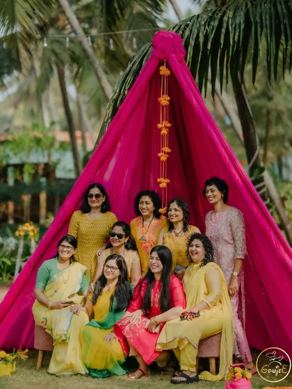 A lovely group photo of guests at a Haldi ceremony, posing in front of a vibrant pink teepee photo booth.