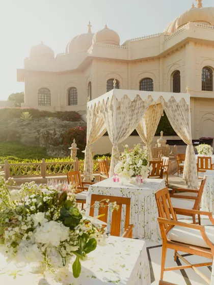 A sun-drenched view of a daytime wedding setup, with elegant canopies and white floral arrangements. The design complements the palace architecture and the natural light.